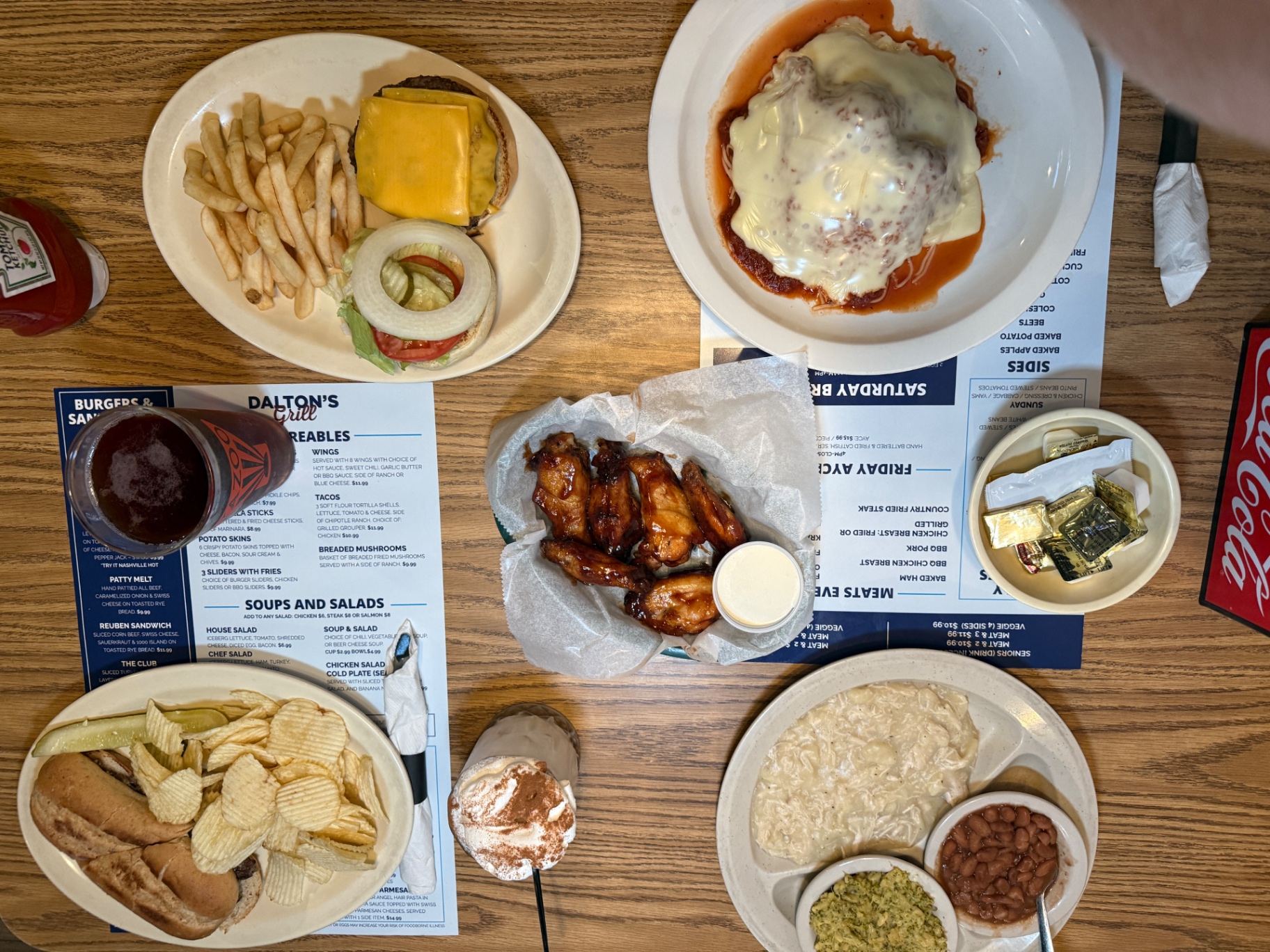 Table spread at Dalton's Grill with a cheeseburger and fries, chicken parmesan, BBQ wings, a meat and three plate, and a milkshake